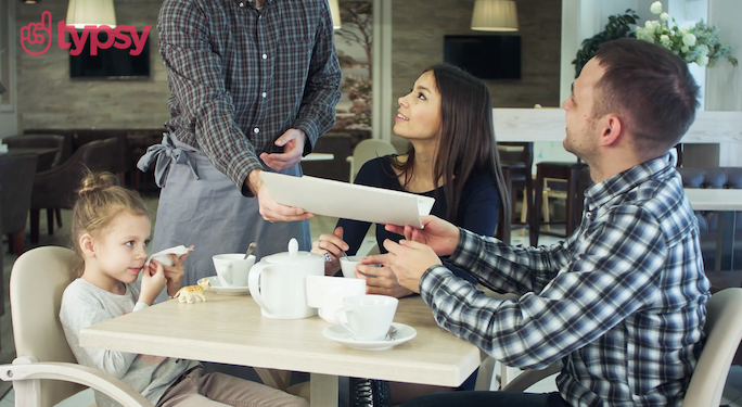 A young couple with a child sit at a restaurant table looking up at their server while being handed a menu.